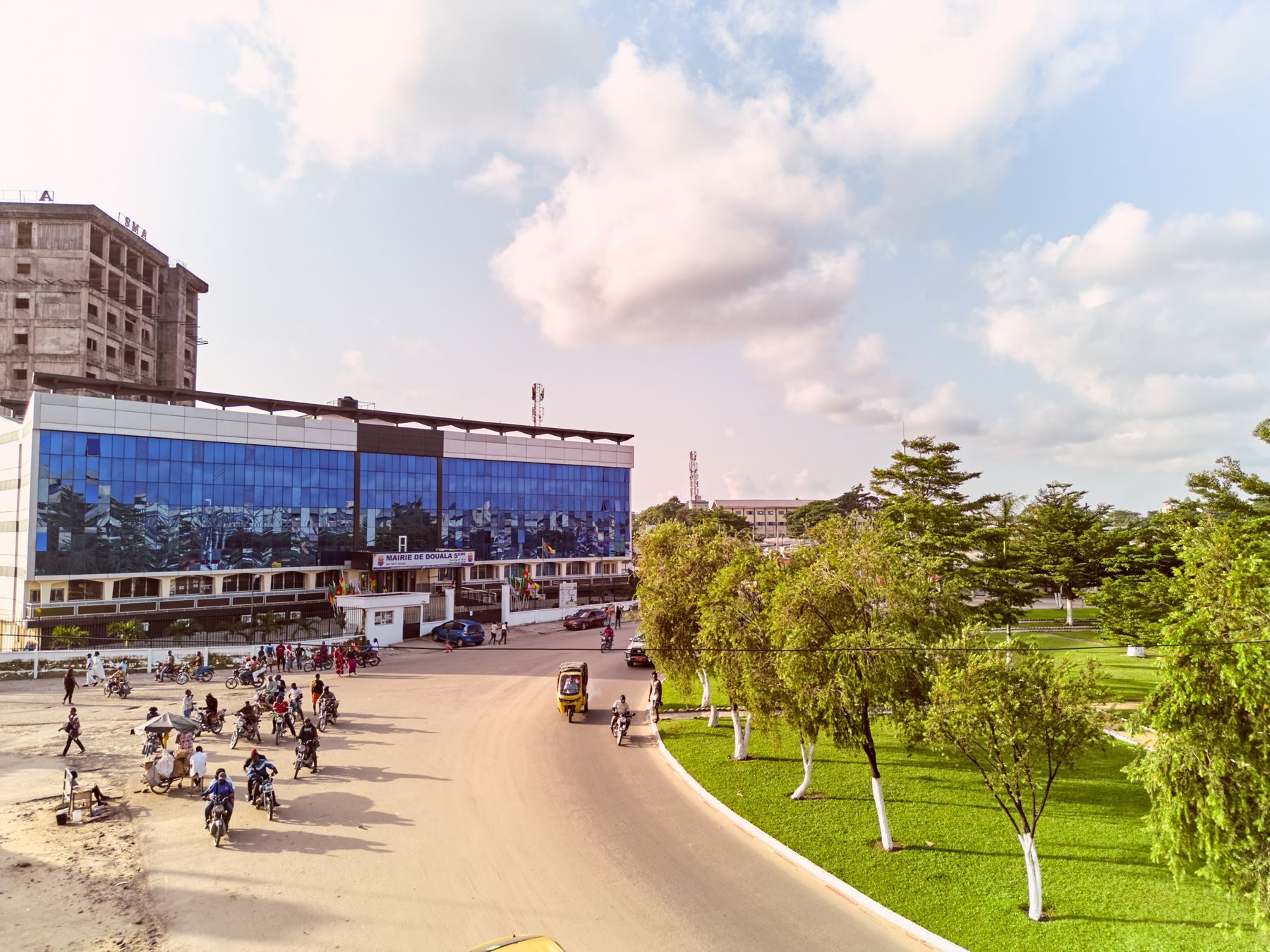 A street in Douala, Cameroon, with motorcyclists passing a modern building.
